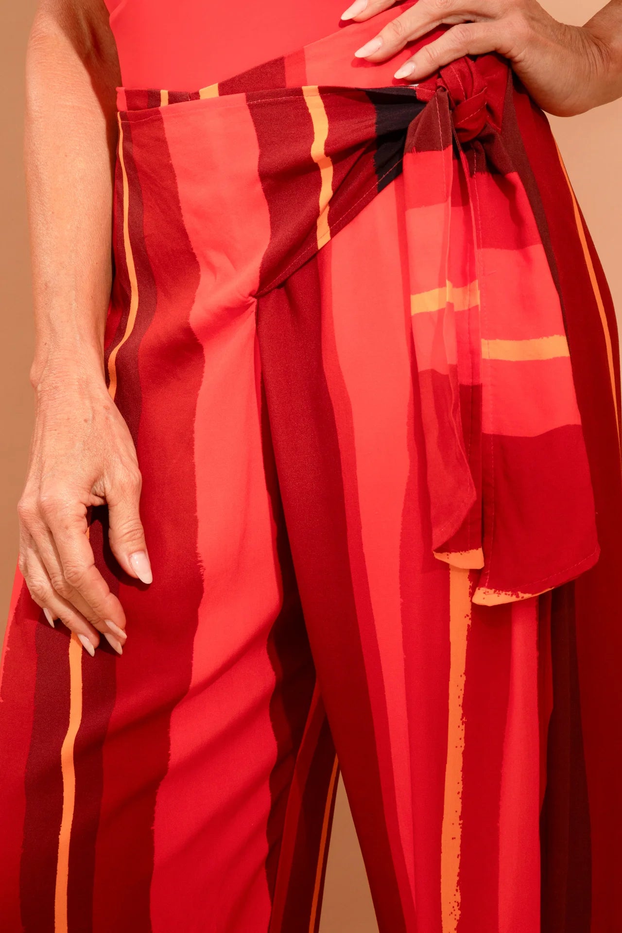 Fotografia de calça modelo pareô pantalona ampla na cor terracota lisa, fecho elegante com laço na cintura, pernas transpassadas e soltas, marca Isa Rodrigues Resortwear. Frente Detalhe